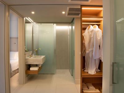 Salle de bain d'hôtel moderne avec lavabo, portes vitrées et armoire ouverte avec peignoirs.