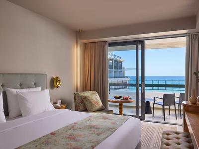 Elegantes Hotelzimmer mit großem Bett, Sitzbereich und Balkon mit Meerblick.