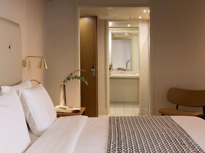 Modernes Hotelzimmer mit großem Bett, Nachttisch und Blick ins Badezimmer.
