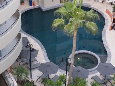 Hotelpool mit geschwungener Form und umgebender Terrasse mit Palmen und Sitzbereichen.