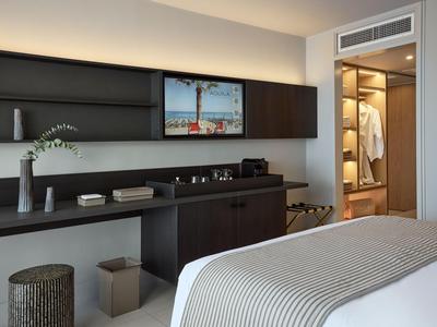 Modern eingerichtetes Hotelzimmer mit großem Bett, Wandregal und begehbarem Kleiderschrank.