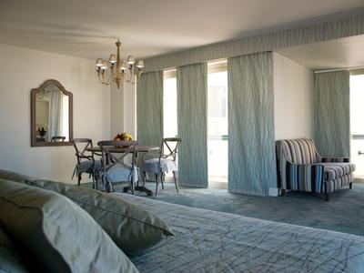 Heller Hotelausblick mit Bett, Esstisch, Stühlen und gemütlichem Sessel am Fenster.