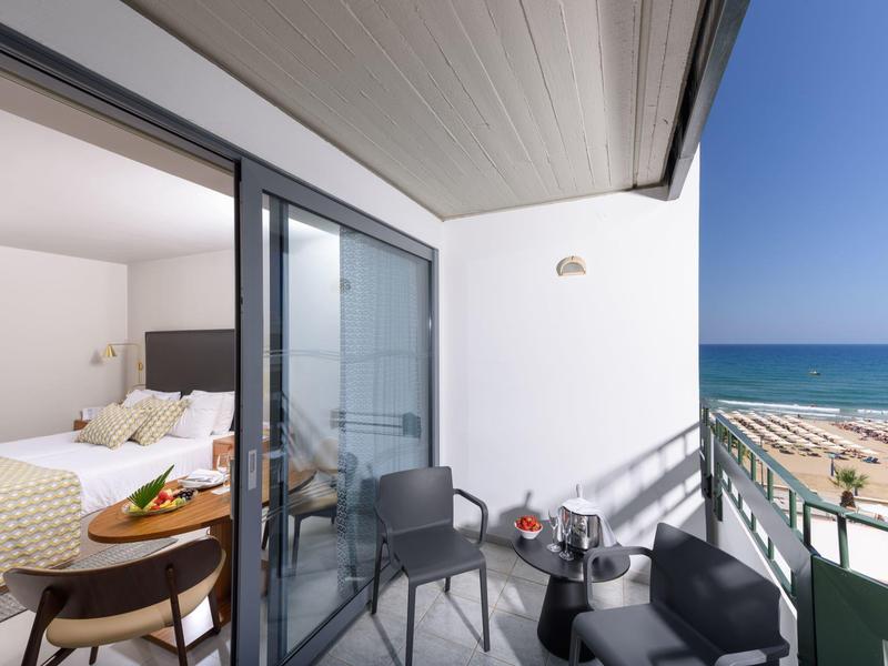 Balcon avec sièges et vue sur la plage, chambre adjacente avec lit.