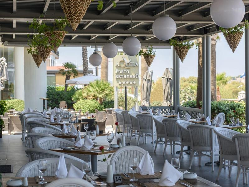 Terrasse couverte avec chaises, tables dressées et pots de plantes suspendus.