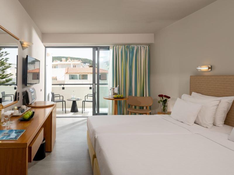 Chambre d'hôtel lumineuse avec grand lit double, bureau et balcon avec vue sur les bâtiments voisins.