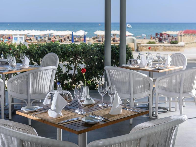 Terrasse de restaurant avec chaises blanches et tables en bord de mer.