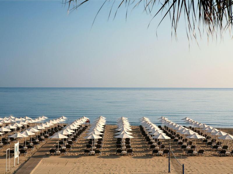 Plage avec rangées de chaises longues et parasols devant une mer calme