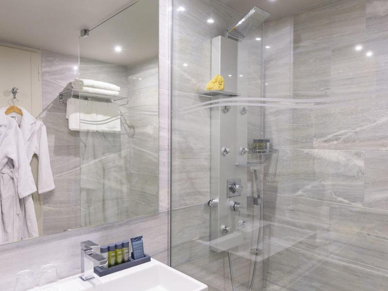 Salle de bain moderne avec douche en verre, peignoirs blancs et serviettes accrochées au mur.