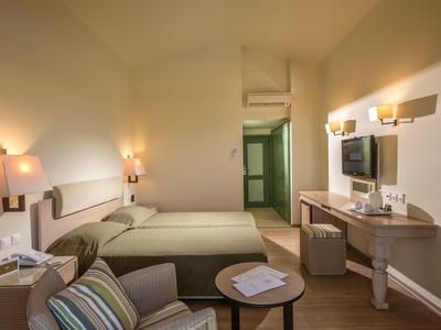 Przytulny pokój hotelowy z dwoma łóżkami, biurkiem z telewizorem, fotelem i miękkim oświetleniem.