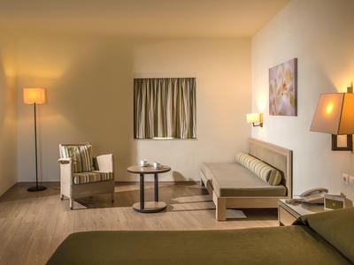 Przytulny pokój hotelowy z ciepłym oświetleniem, miejscem do siedzenia, łóżkiem i neutralnym wystrojem.