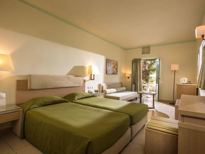 Pokój hotelowy z dwoma łóżkami, zieloną pościelą, lampami i drzwiami na balkon.