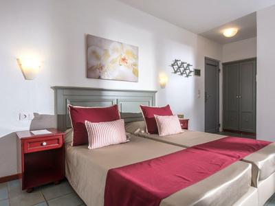 Nowoczesny pokój hotelowy z dwoma łóżkami pojedynczymi, czerwonymi akcentami, stolikiem nocnym i obrazem na ścianie.