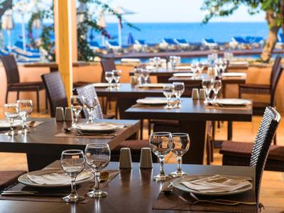 Stoły restauracyjne na zewnątrz nakryte szkłem i sztućcami z widokiem na morze i łodzie.