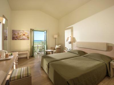 Jasny pokój hotelowy z dwoma pojedynczymi łóżkami, balkonem i widokiem na morze.