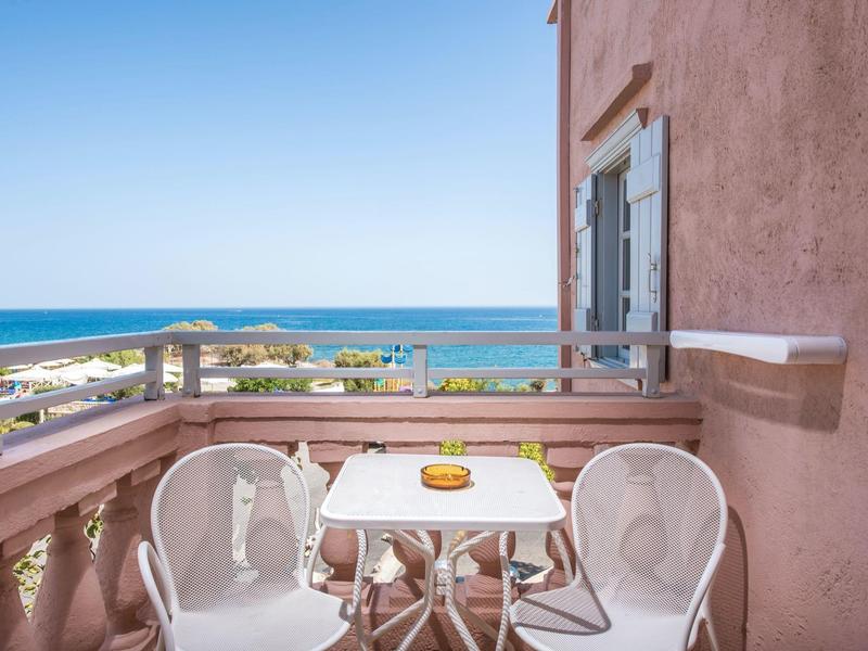 Balkon z dwoma białymi krzesłami i stołem z widokiem na morze w słoneczny dzień.