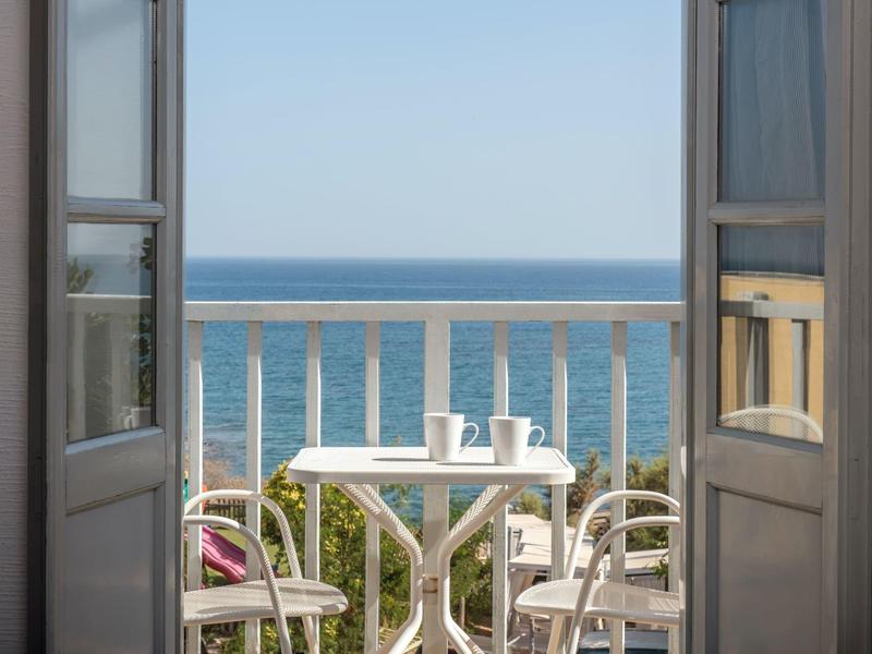 Balkon z stołem, krzesłami i kubkami z widokiem na spokojne morze pod czystym niebem.