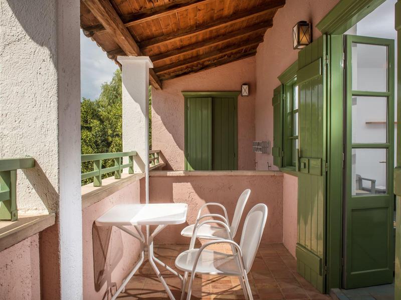 Przytulny balkon z białym stołem, krzesłami i zielonymi drzwiami pod drewnianym dachem.