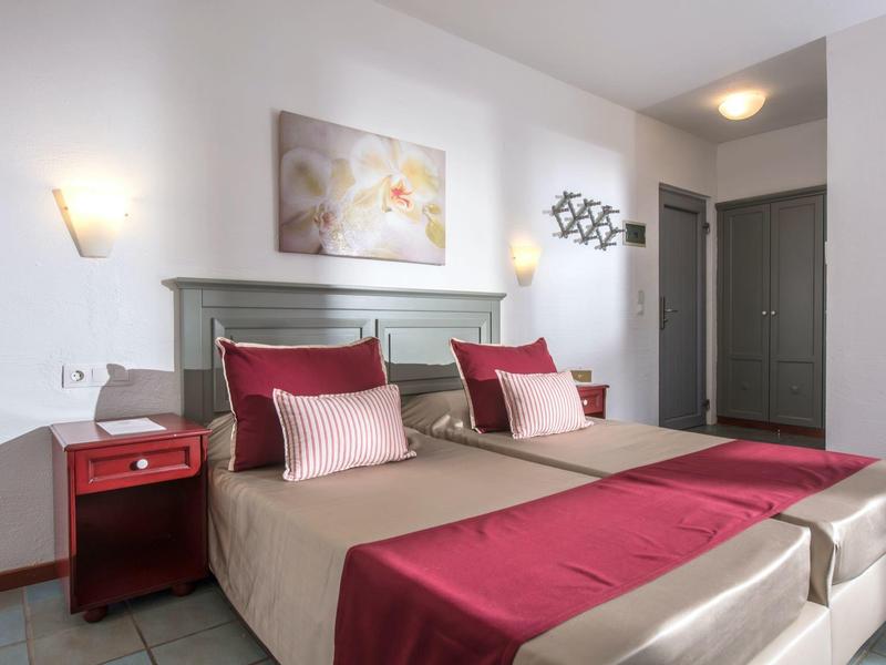 Nowoczesny pokój hotelowy z dwoma łóżkami pojedynczymi, czerwonymi akcentami, stolikiem nocnym i obrazem na ścianie.