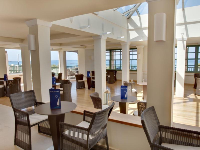 Jasny salon hotelowy z wiklinowymi krzesłami i stołami pod dużymi oknami i świetlikami.