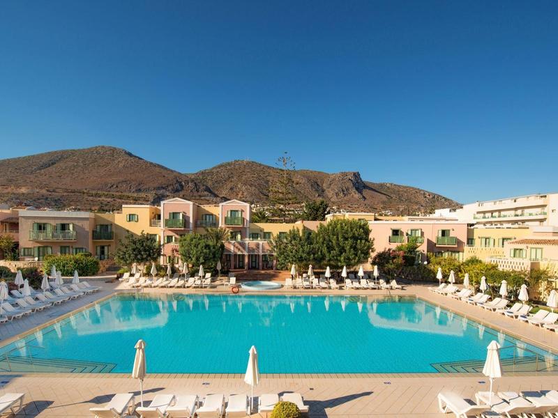 Duży prostokątny basen na zewnątrz z leżakami i parasolami pod jasnym niebem.