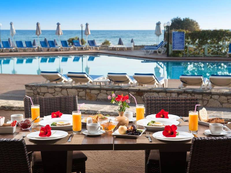 Stół śniadaniowy z jedzeniem i napojami przy basenie z widokiem na morze w ośrodku.