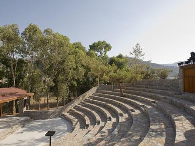 Venkovní kamenné amfiteátr s stupňovitým sezením obklopený stromy a kopci v pozadí.