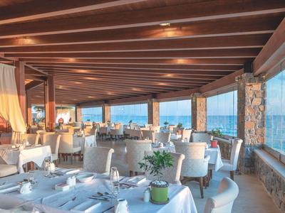 Pohodlná restaurace s dřevěným trámovým stropem a velkými okny s výhledem na moře.