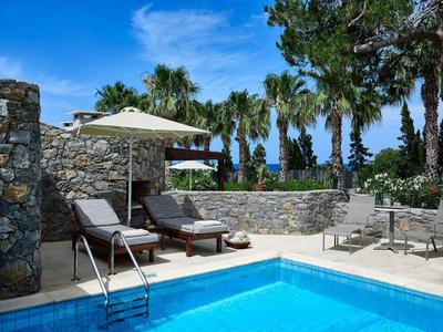 Zona de piscina al aire libre con tumbonas, sombrillas y palmeras bajo un cielo azul despejado.