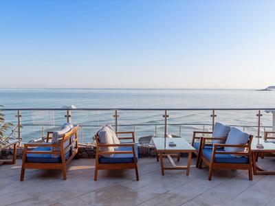 Terrasse mit Holzsesseln und Tisch mit Blick auf das Meer bei klarem Himmel.