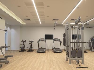 Moderní posilovna s běžeckými pásy, koly a fitness vybavením na světlé dřevěné podlaze.
