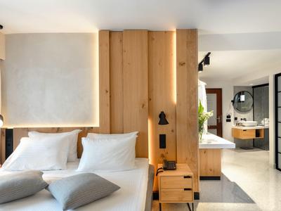 Habitación de hotel moderna con detalles de madera, cama con almohadas blancas y luz en la pared.