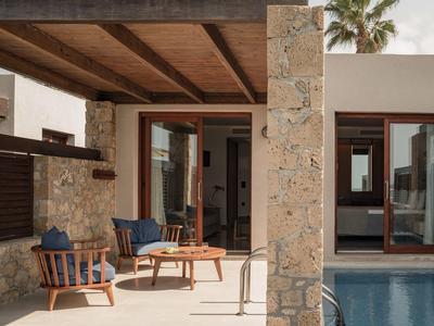 Terraza con muebles de madera y piscina junto a una casa moderna con paredes de piedra.