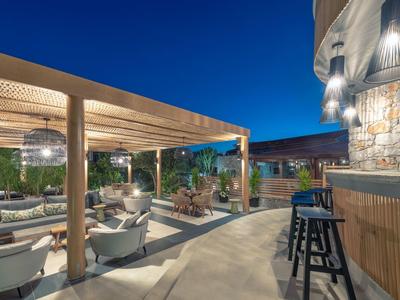 Lounge exterior nocturna con pérgola de madera, grupos de asientos y bar en terraza de hotel bajo cielo despejado.