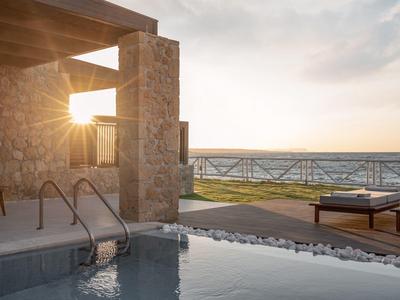 Área moderna de piscina con tumbonas y vista al mar al atardecer.