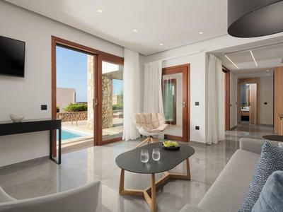 Sala moderna con acceso a la piscina, sofá, mesa de centro y grandes ventanales en un hotel.