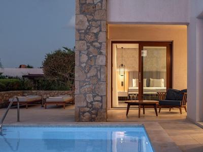 Área exterior moderna con piscina iluminada, fachada de piedra y cómodo conjunto de asientos al atardecer.