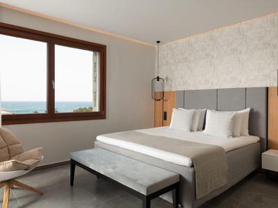 Habitación de hotel moderna con cama grande, área de asientos y vista al mar desde la ventana.