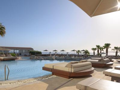 Moderní bazénová zóna s lehátky, slunečníky a palmami pod jasnou oblohou.