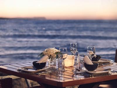 Prostřený dřevěný stůl se sklenicemi a ubrousky u klidného moře při západu slunce.