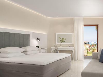 Habitación de hotel luminosa con cama grande, escritorio y vista al mar.