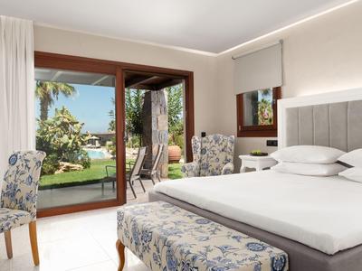 Elegante habitación de hotel con cama grande y vista al jardín a través de puerta corredera de vidrio.