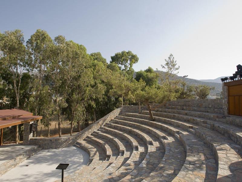 Un anfiteatro abierto con filas de asientos de piedra en forma de semicírculo rodeado de árboles y montañas al fondo.