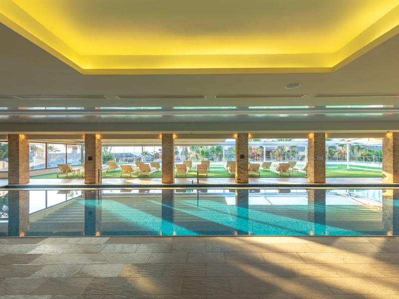 Área interior de una gran piscina con ventanales panorámicos y vista a zonas exteriores.