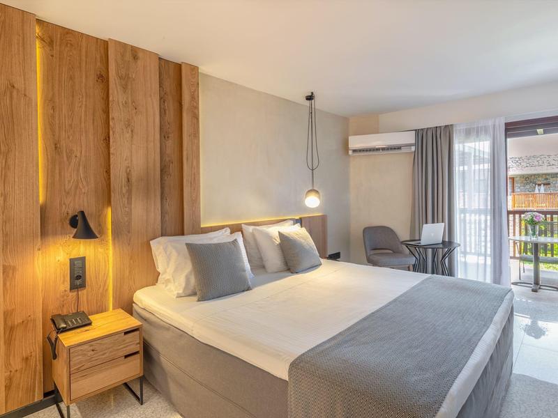 Habitación de hotel moderna con cama grande, pared de madera, mesita y balcón con vista exterior.