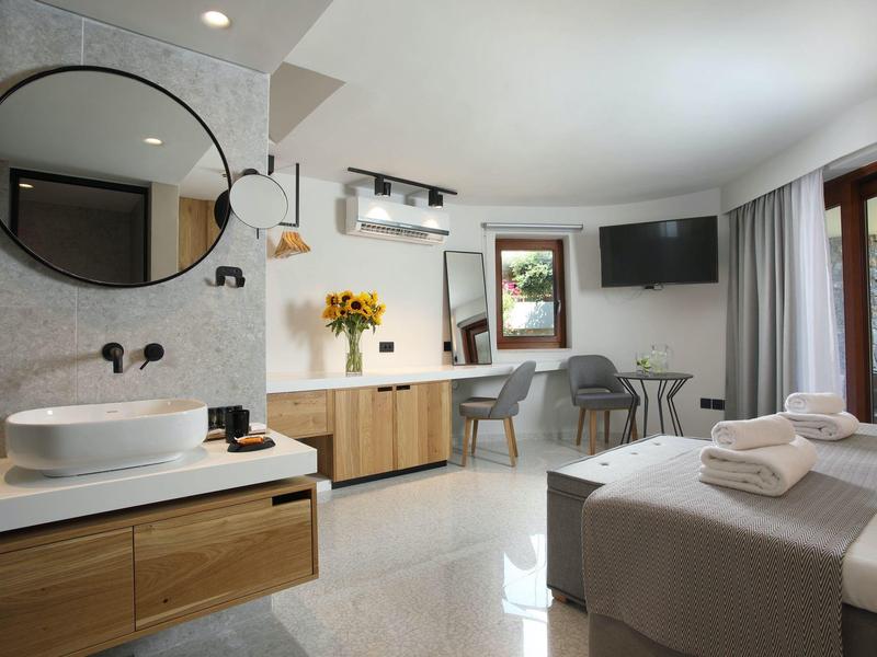 Habitación de hotel luminosa con cama doble, área de baño con lavabo y espejo grande, decoración moderna.