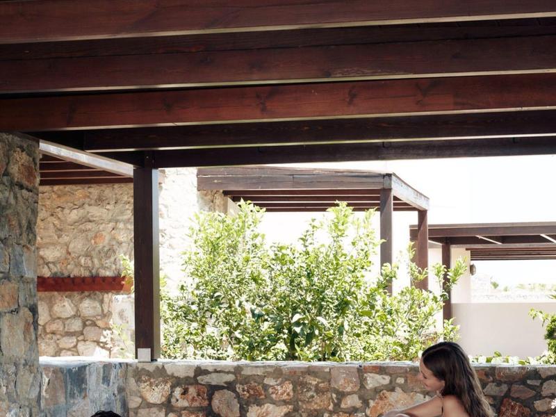 Dos personas descansan en el área exterior de un hotel con muros de piedra y vigas de madera.