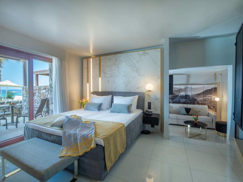 Habitación de hotel moderna con cama doble, banco, balcón y suelo claro.