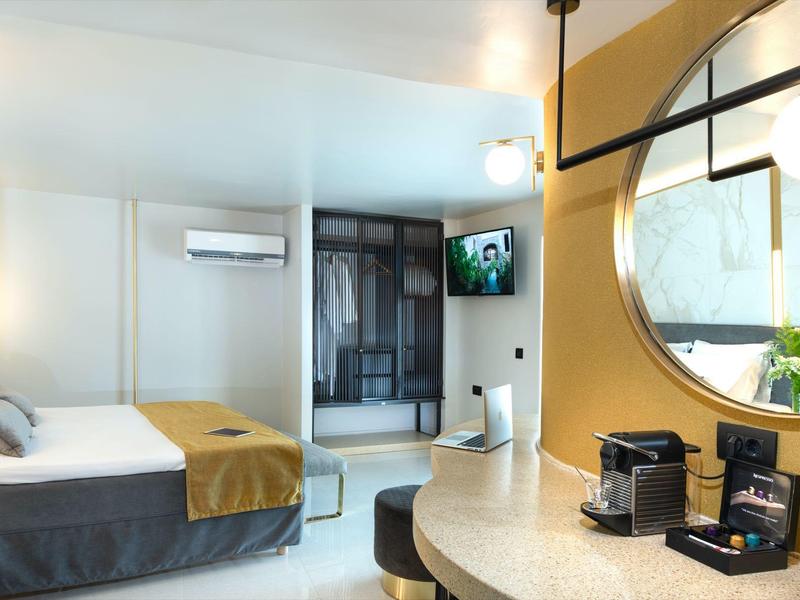 Habitación de hotel moderna con cama doble, escritorio, espejo y cafetera bajo luz cálida.