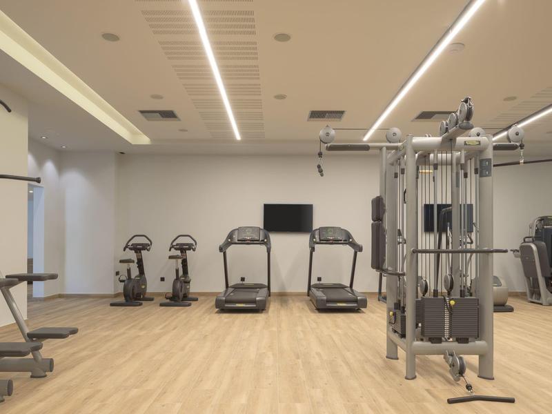 Gimnasio moderno en el hotel con cintas de correr, bicicletas y equipos de fuerza sobre suelo de madera clara.