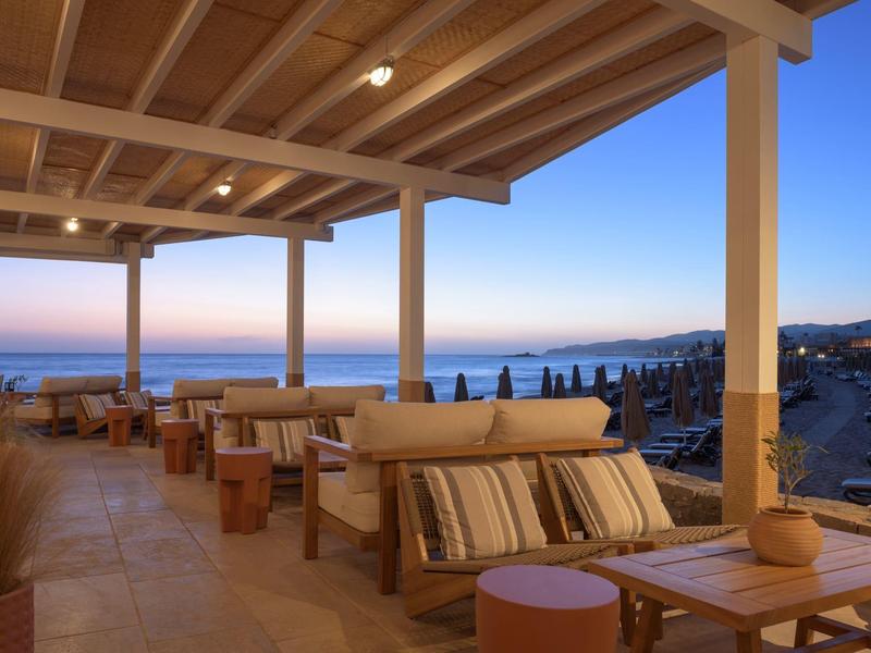 Terraza cubierta con cómodas áreas de asiento, vista al mar al atardecer.